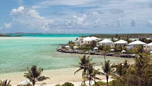 Un resort frente a la playa con bungalows sobre el agua, aguas turquesas cristalinas y palmeras.