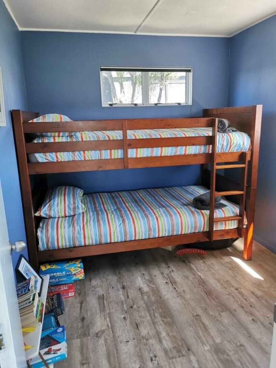 A bunk bed room with blue walls, a window, and a wooden floor.