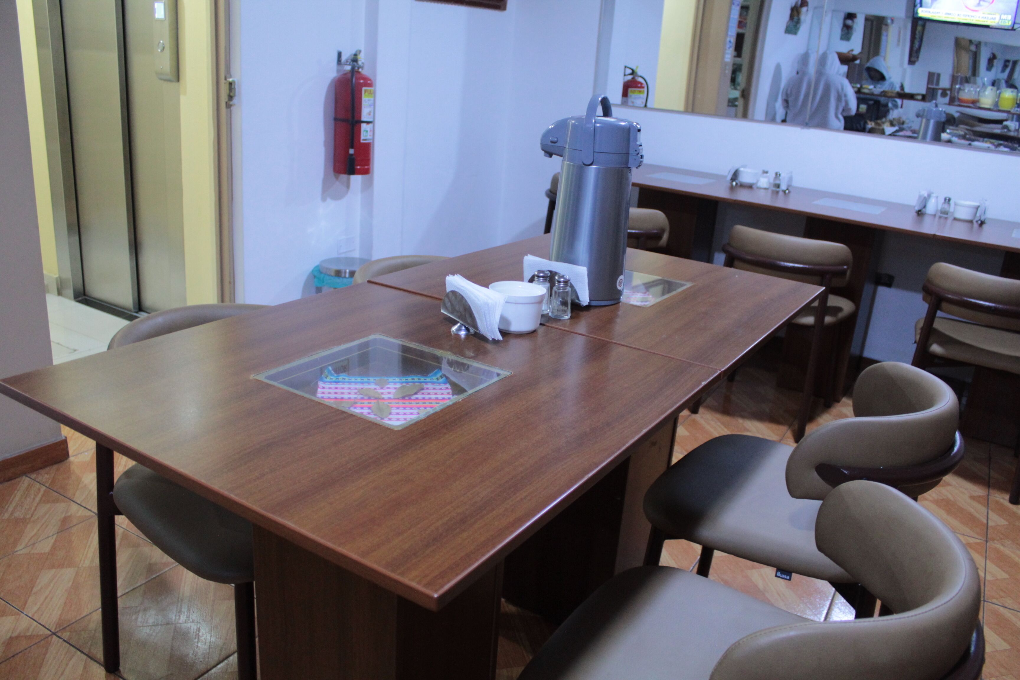 Una sala de conferencias con una mesa de madera, cuatro sillas, una máquina de café, un extintor y suelo de baldosas.