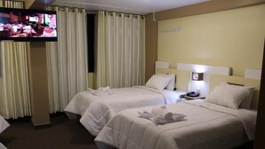 Et hotelværelse med to senge, et fjernsyn og et natbord med telefon.