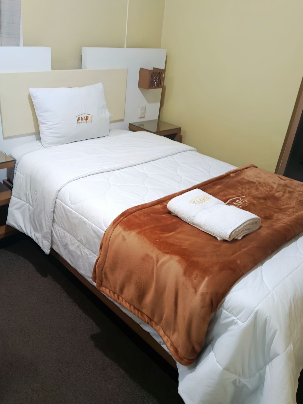 A hotel room with a bed, a nightstand, and a wall-mounted mirror.