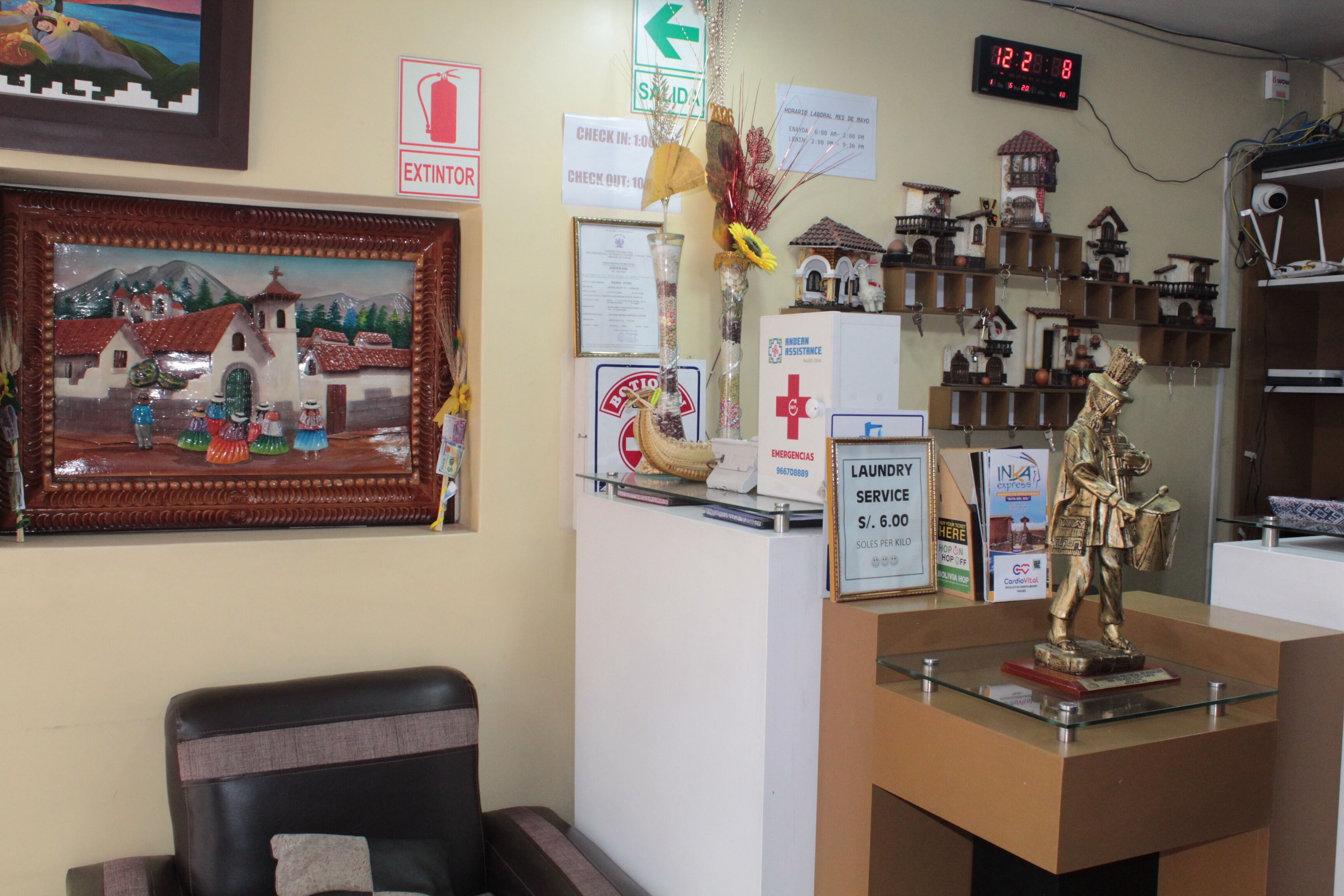 Un área de recepción con un cuadro enmarcado, un reloj, una estatua y varios letreros, incluyendo un cartel de servicios de emergencia.