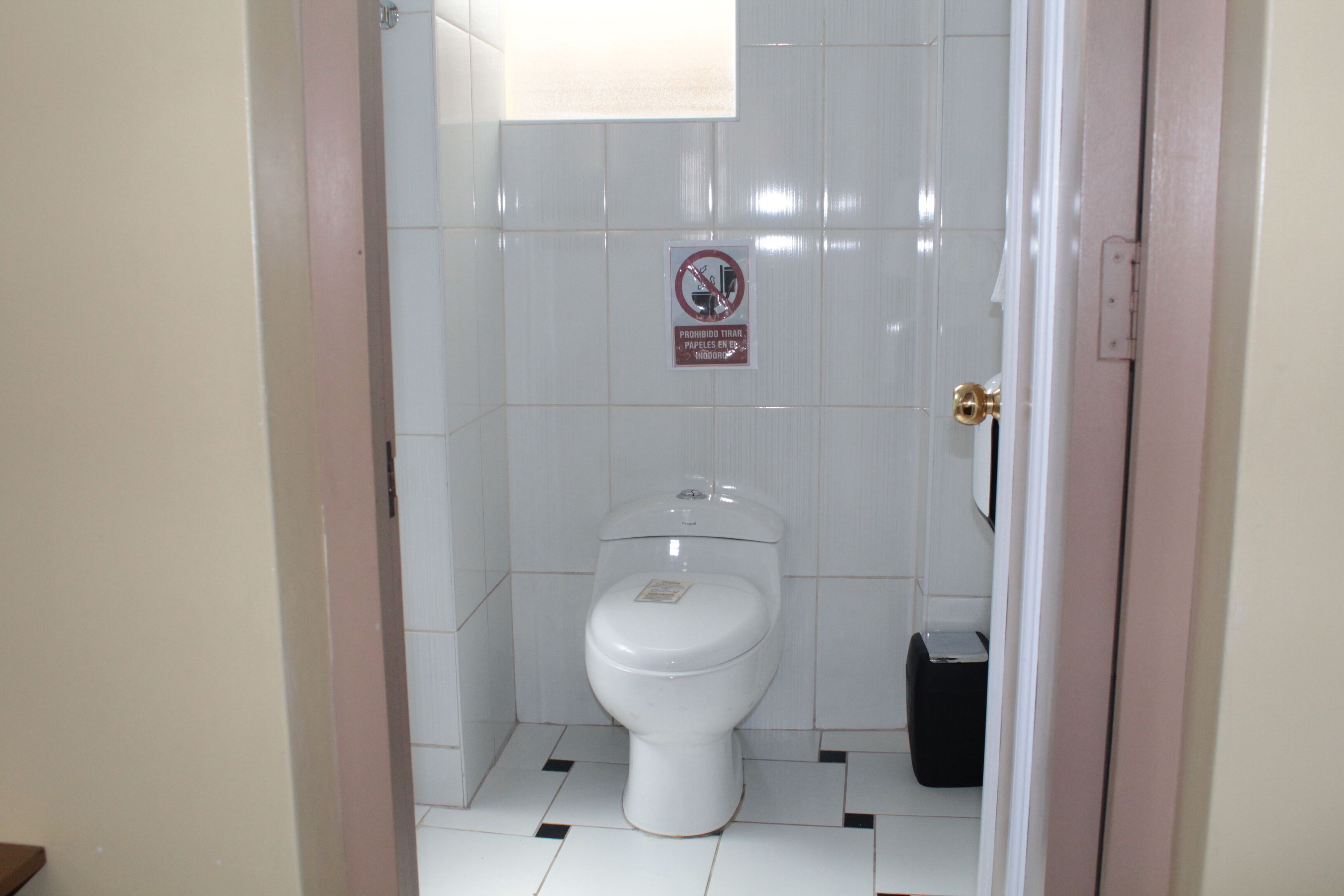 Une salle de bain équipée de toilettes, d’une poubelle et d’un panneau « défense de fumer » sur le mur.