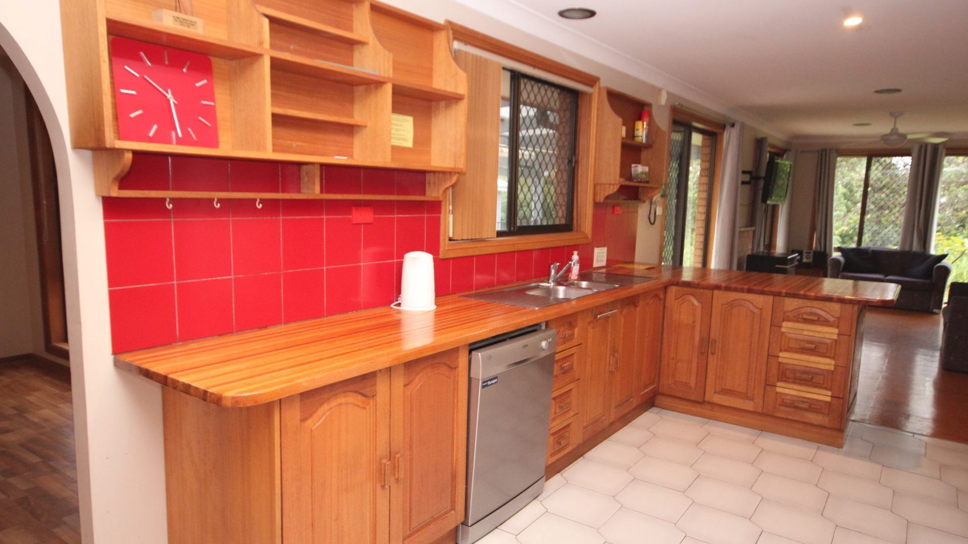 A kitchen with wooden cabinets, a stainless steel dishwasher, and a red tiled backsplash.