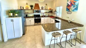 Una cocina moderna con encimera de granito, armarios blancos, horno empotrado e isla central con taburetes de bar.