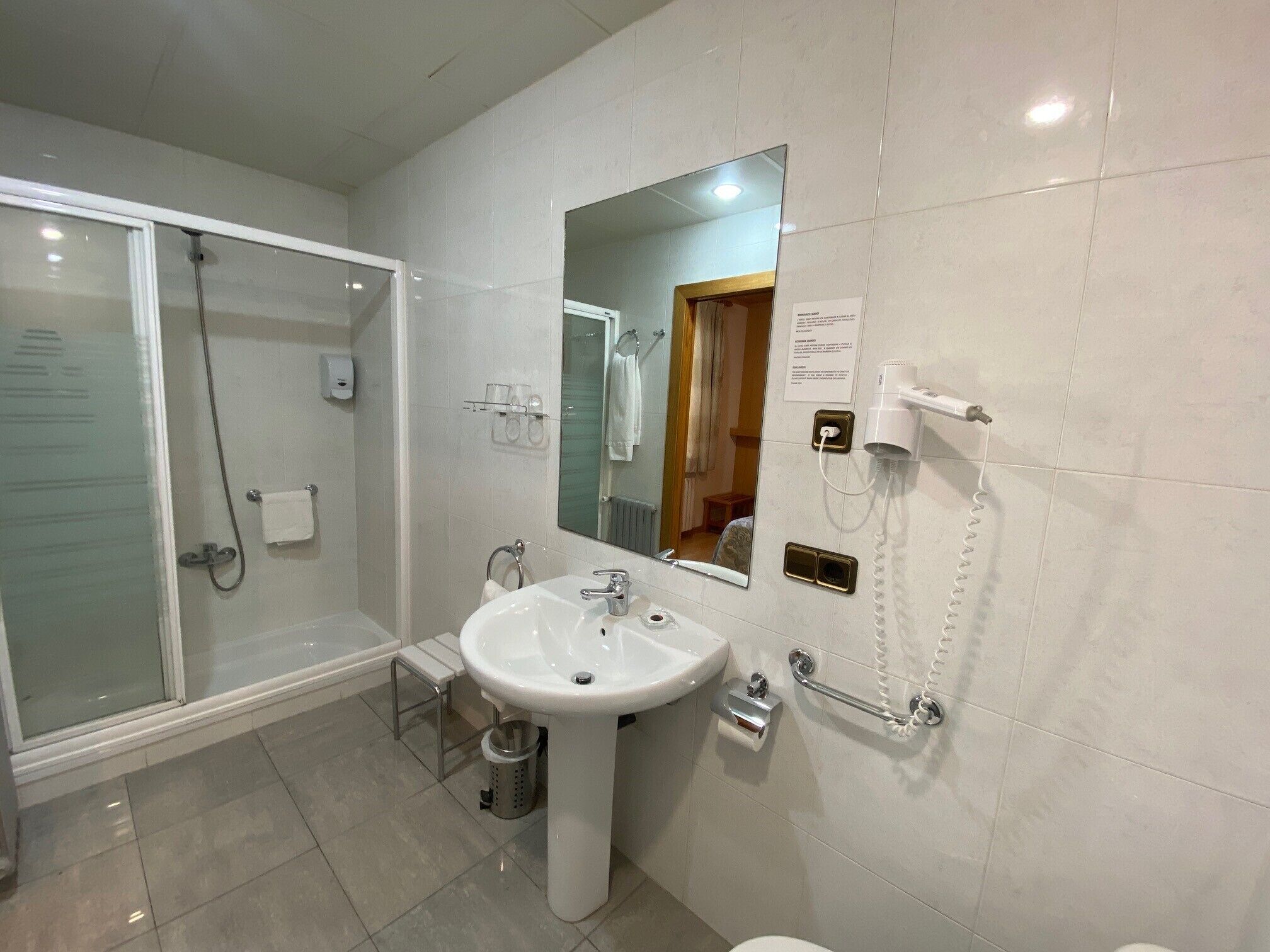 Een moderne badkamer met een glazen douchecabine, een wastafel op een zuil en een spiegel met ingebouwde verlichting.
