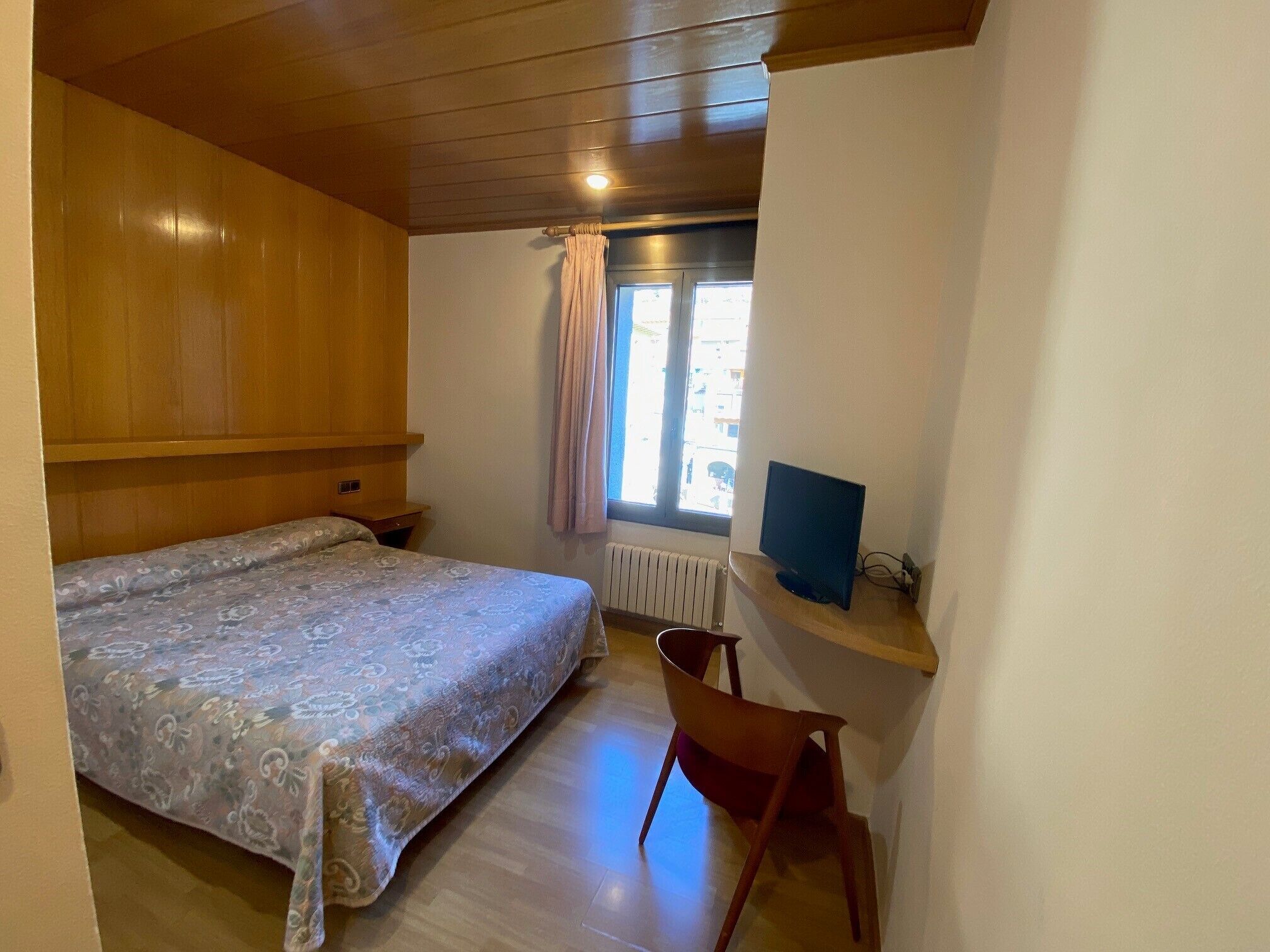 Un dormitorio pequeño y acogedor con cama, una silla, escritorio con computadora y ventana con cortinas.