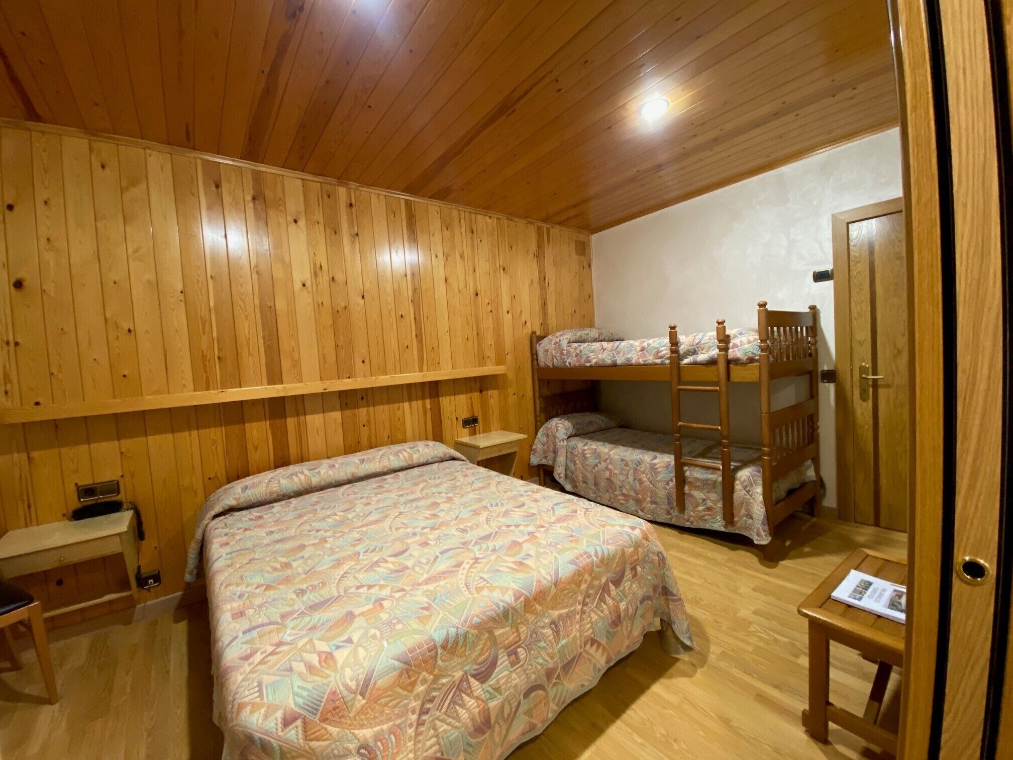 A wooden-paneled room with bunk beds, a desk, and a small table.