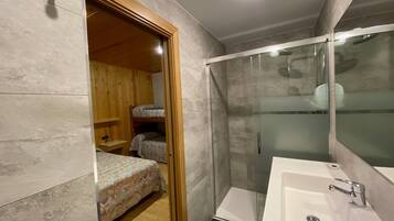 A modern bathroom with a glass-enclosed shower, a large white sink, and a wooden door leading to a bedroom with bunk beds.