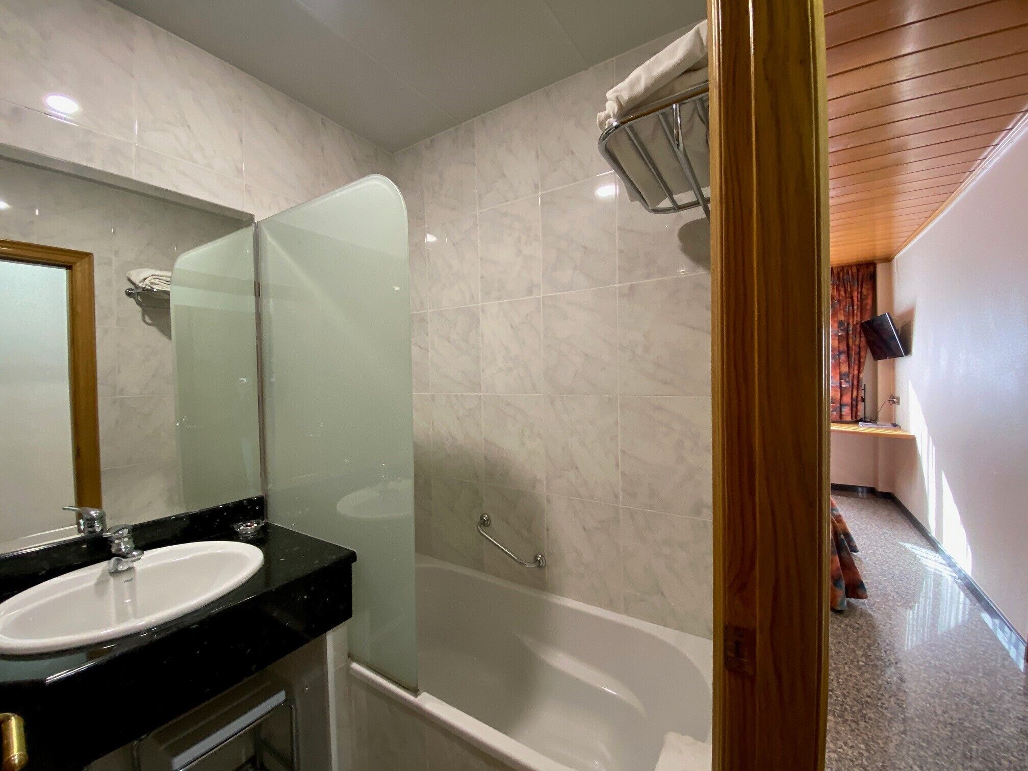 Un baño moderno con ducha de vidrio, lavamanos blanco y tocador de madera.