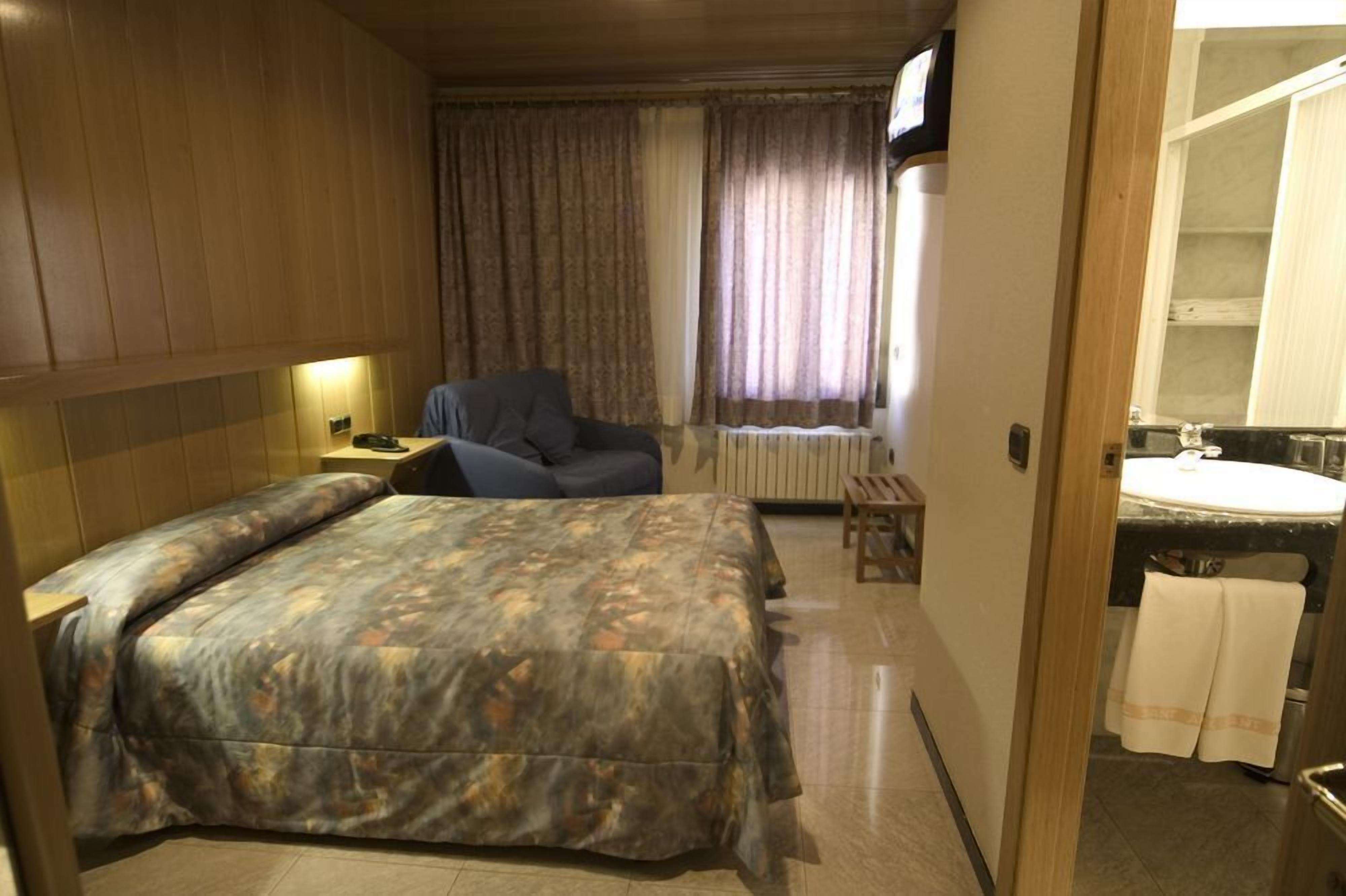 Ein Hotelzimmer mit Bett, Stuhl, Schreibtisch, Spiegel und Badezimmer.