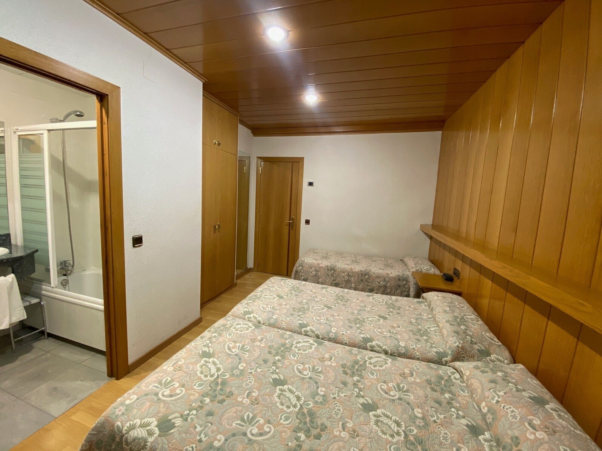 A bedroom with two beds, a wooden wardrobe, a bathroom with a shower, and a small table.