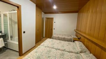 A bedroom with two beds, a wooden wardrobe, a bathroom with a shower, and a small table.