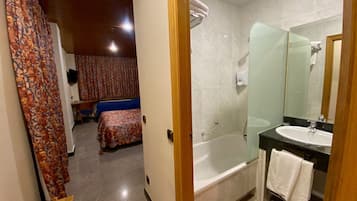 Een hotelkamer met een bed, een badkamer met een bad, een wastafel en een spiegel.