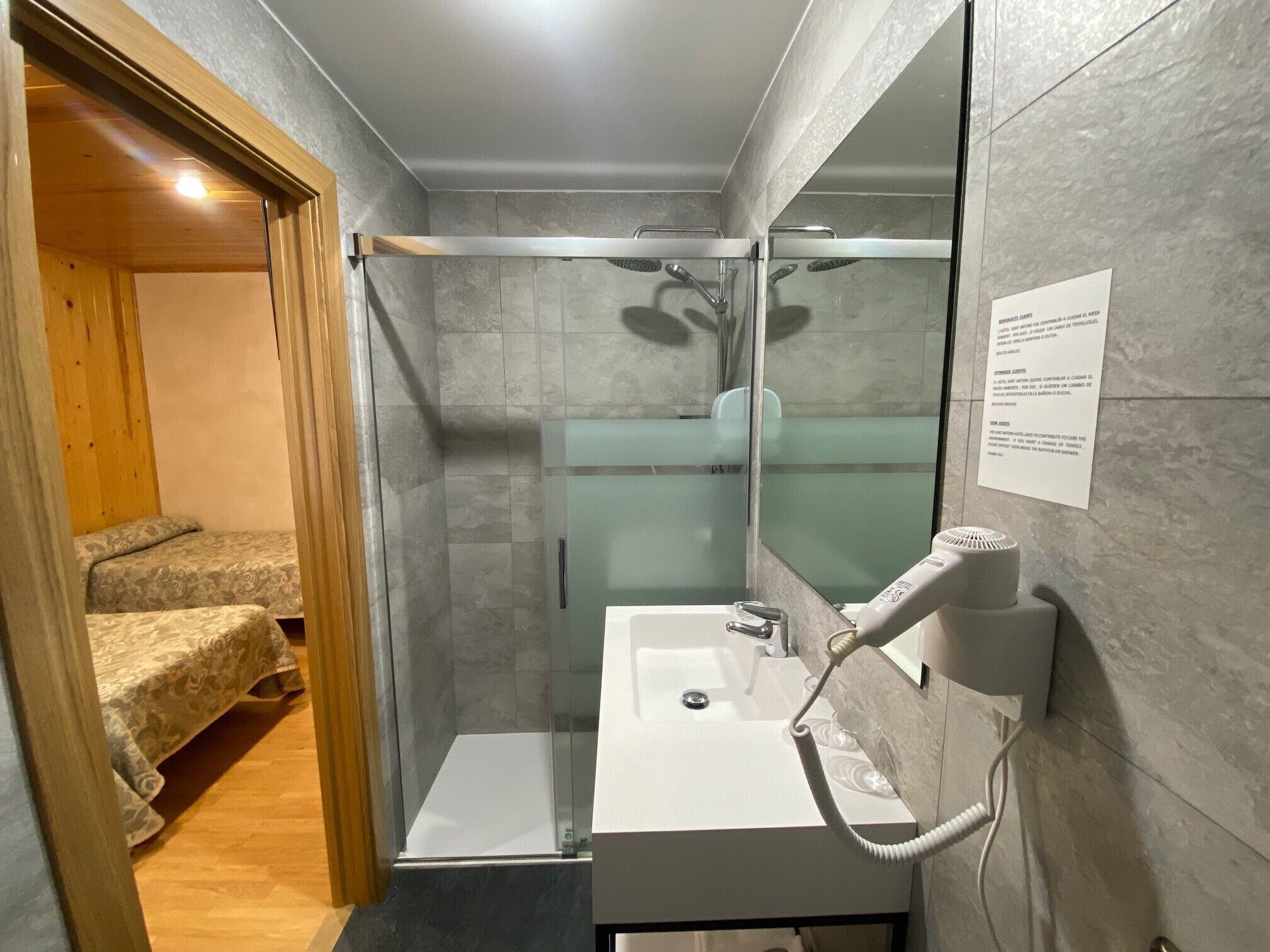 Un baño moderno con cabina de ducha de vidrio, un lavabo blanco y un secador de pelo en la pared.