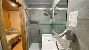 Un baño moderno con cabina de ducha de vidrio, un lavabo blanco y un secador de pelo en la pared.