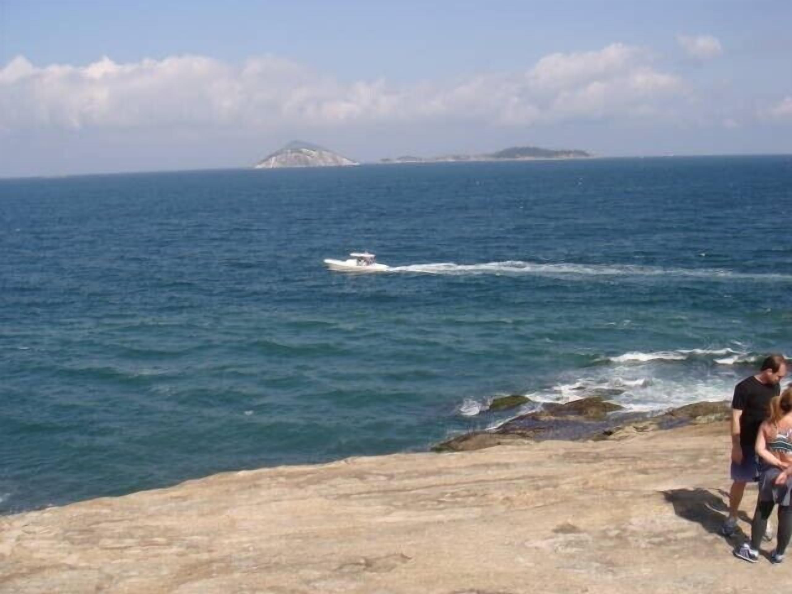 A rocky coastline with a boat on the water and a distant island.