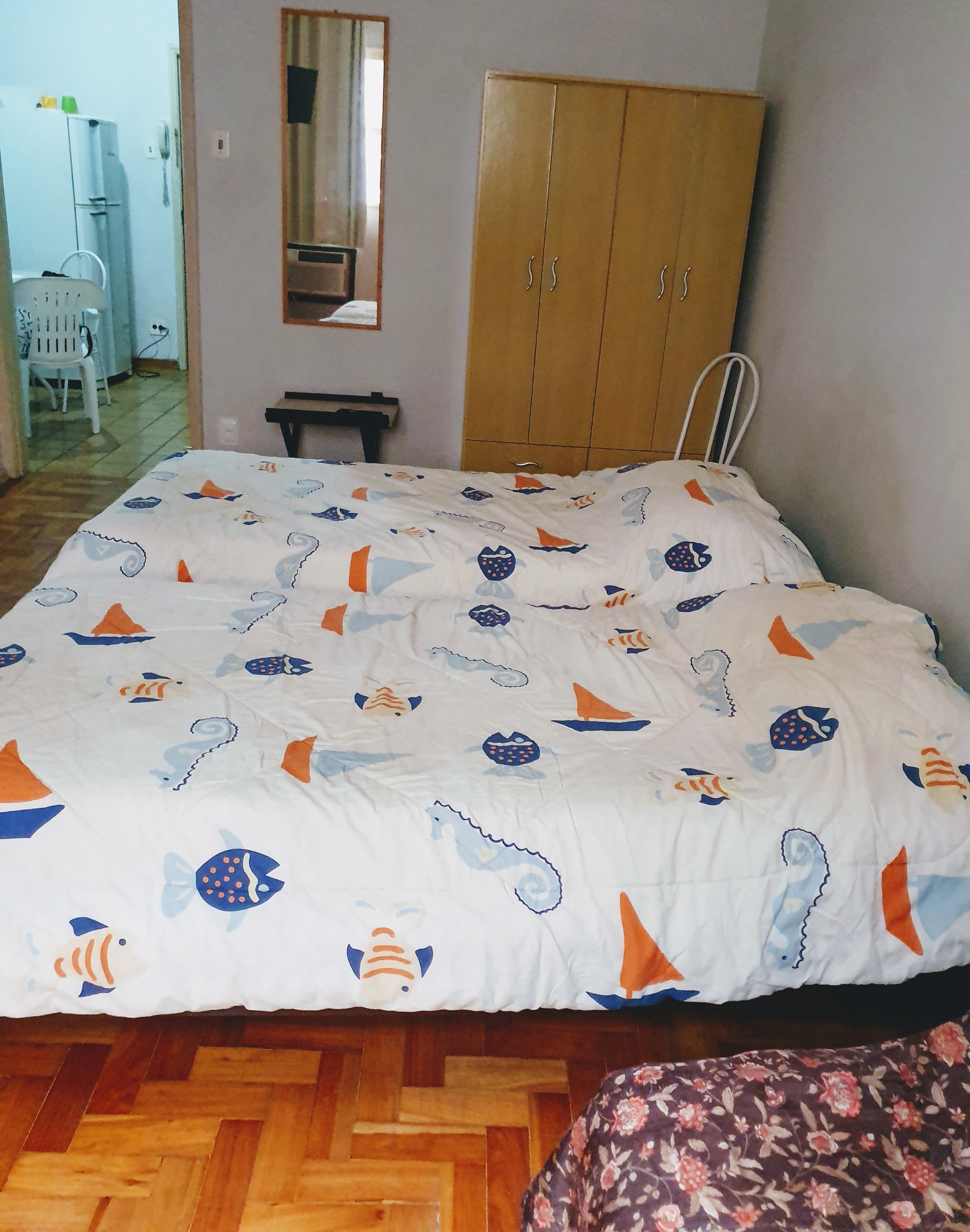 Ein Schlafzimmer mit einem Bett, das mit einer marineblauen Bettdecke bezogen ist, einem Holzschrank, einem kleinen Tisch und einem Stuhl.