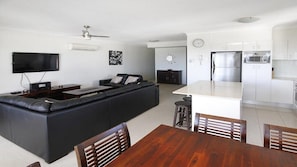 Un espacio habitable moderno con un sofá seccional negro, una mesa de comedor de madera y una cocina con armarios blancos y electrodomésticos de acero inoxidable.