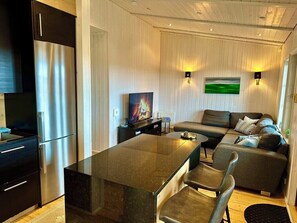 Eine moderne Küche mit einem Edelstahl-Kühlschrank, einem Esstisch mit Stühlen, einer Couch und einem Fernseher.