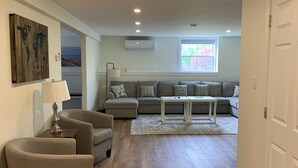 Un salón amplio con suelo de madera, un sofá gris, una mesita de centro y una lámpara.