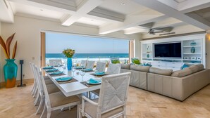 Zona pranzo con vista sull'oceano, una TV e un angolo salotto con divano e poltrone.