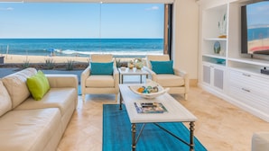 Un soggiorno con vista sulla spiaggia, un ventilatore a soffitto, una TV e un'area pranzo.