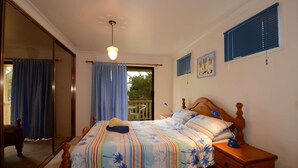 A bedroom with a bed, a nightstand, a mirror, and a window with curtains. - Seahaven Beach House - This brilliant beach house sleeps up to 8 adults and 2 children. (shellharbour)
