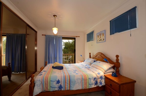 Un dormitorio con cama, mesita de noche, espejo y ventana con cortinas.