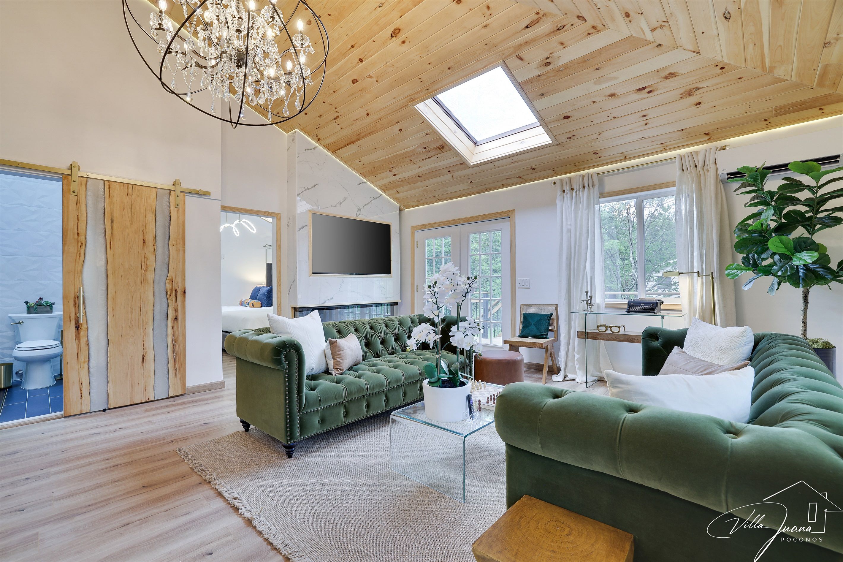 A spacious living room with a green sofa, a glass coffee table, and a chandelier.