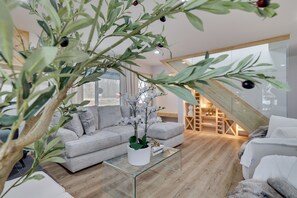 A modern living room with a glass coffee table, grey sofa, and a staircase leading to an upper level. - Luxury Poconos Getaway | Hot Tub, Fire Pits, Game Room, EV Charger & King Beds (Tobyhanna)