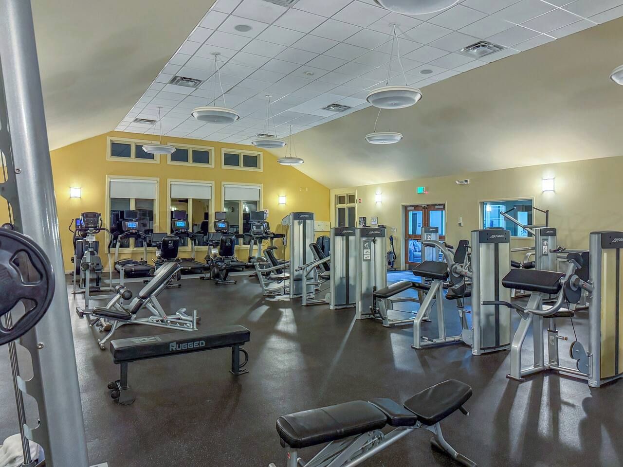 Un gimnasio con equipos de ejercicio variados, incluyendo cintas de correr, máquinas de pesas y una banca.