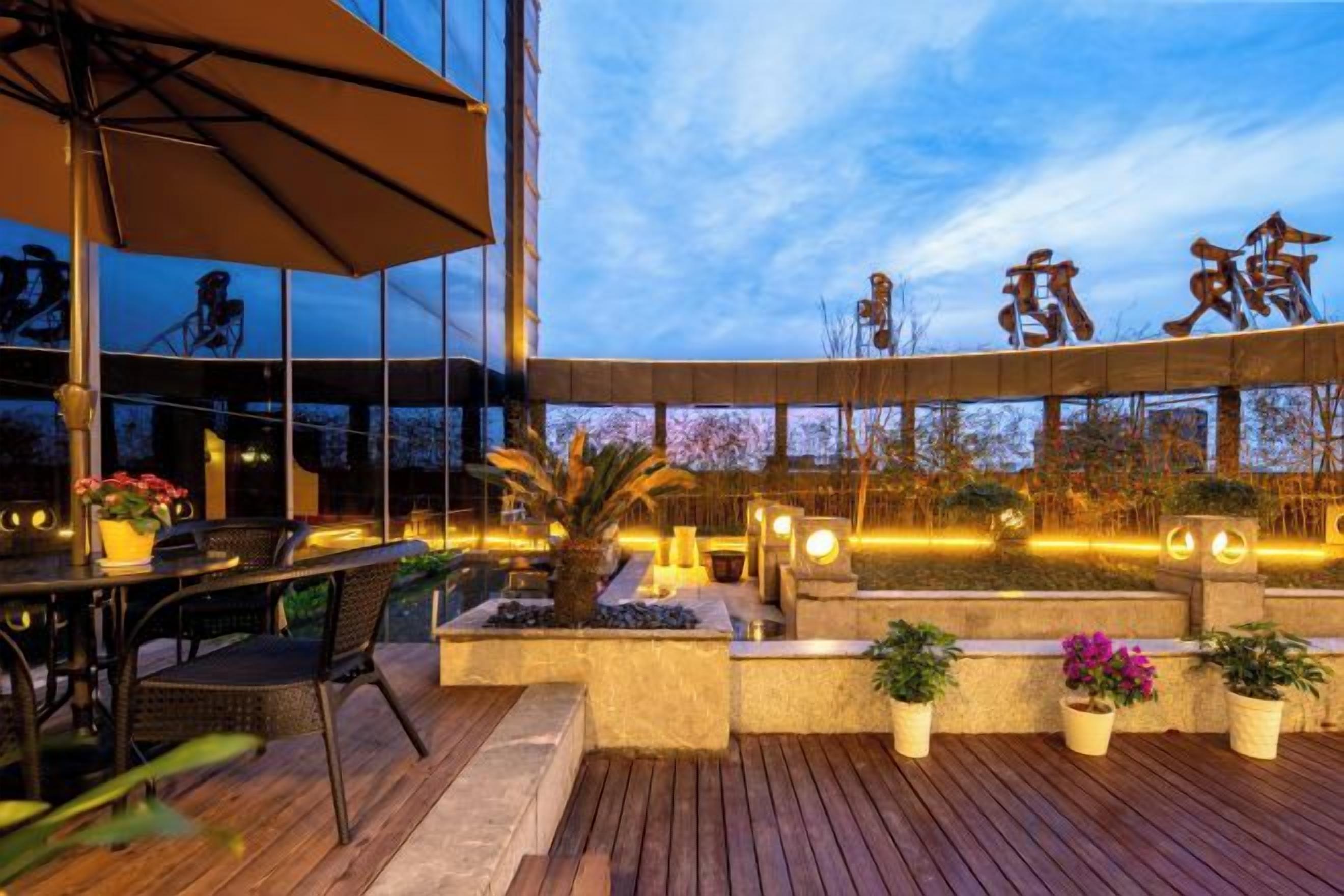 An outdoor seating area with tables and chairs, a wooden deck, and potted plants.