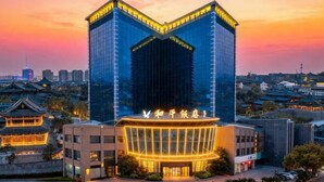 A modern hotel with a distinctive curved facade, a traditional building adjacent to it, and a cityscape in the background. - Heping Hotel (Tongxiang)