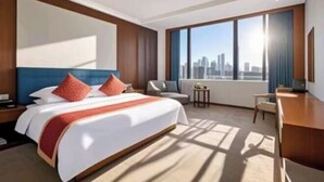 A hotel room with a large bed, a desk, a chair, and a view of a city skyline. - Heping Hotel (Tongxiang)