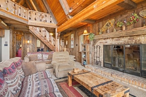 Een rustiek interieur met een open haard, houten trap en een zithoek.
