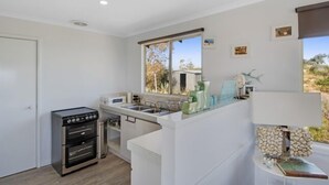 A compact kitchen with a built-in oven, a sink, and a window overlooking a natural landscape. - Serindipity - 180 Degrees ocean view (Yanchep)
