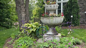 A stone fountain with flowers in a garden with a stone house in the background. - Elegant Vacation Home in picturesque Jackson NH perfect for reunions, gatherings (Jackson)