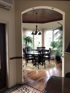 A dining area with a round table, dark chairs, a patterned rug, and potted plants.