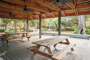 Terraza de madera exterior con mesas de picnic y ventiladores de techo.