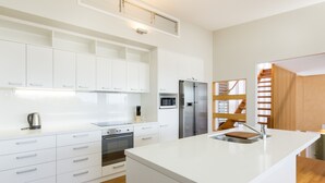 A modern kitchen with white cabinetry, stainless steel appliances, and a wooden staircase.