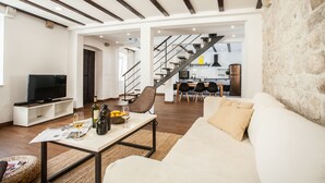 Una sala de estar moderna con un sofá, una mesa de centro y un televisor. Se ve una escalera que sube a un piso superior.