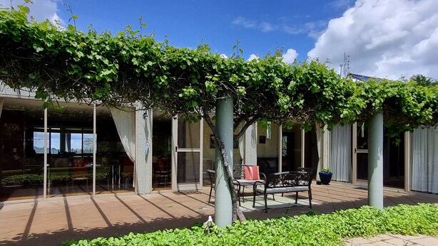 Un espacio al aire libre cubierto con una pérgola, asientos y vista al interior del edificio.