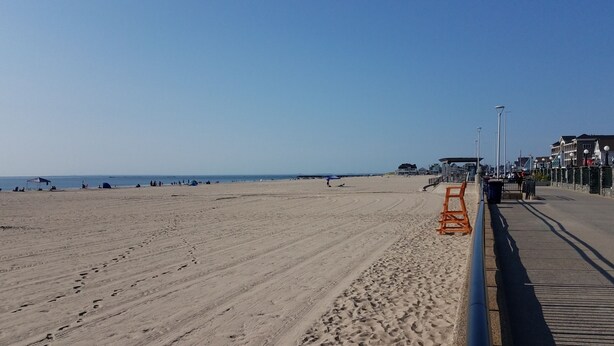 Ein weiter Sandstrand mit einer Promenade, Strandkörben und einem Rettungsschwimmerstand.