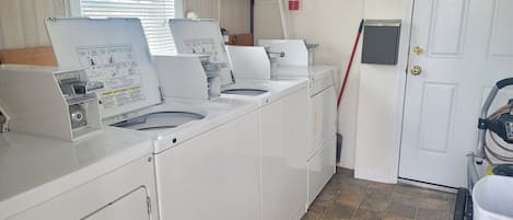 A laundry room with multiple washing machines, a fire extinguisher, a clock, and a door with a key lock.