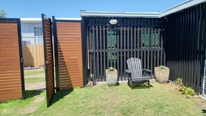 Une cour arrière clôturée avec une porte en bois, une chaise noire et deux jardinières.
