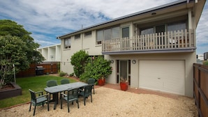 A two-story residential building with a balcony, a covered garage, and a patio area with a table and chairs. - Banksia Seven - Merimbula (Merimbula)