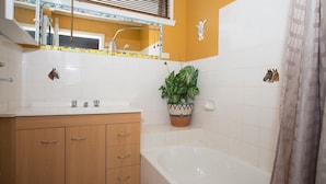 A bathroom with a wooden vanity, a white bathtub, and a potted plant. - Banksia Seven - Merimbula (Merimbula)