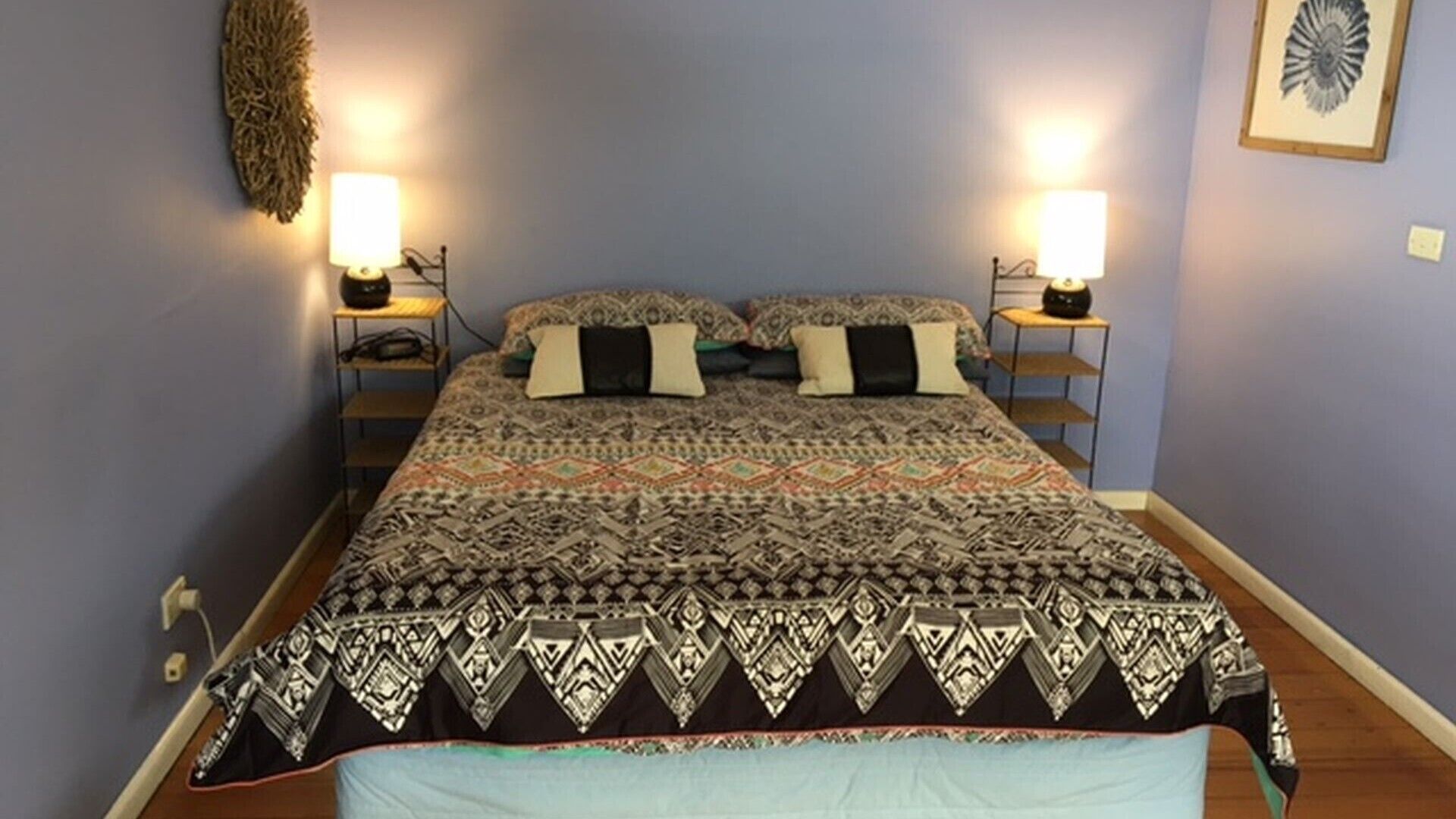 A bed with a patterned bedspread, two bedside lamps, and a wall-mounted decorative piece.