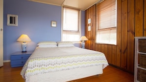 A bedroom with a bed, two bedside tables with lamps, a dresser, and wooden walls. - Banksia Seven - Merimbula (Merimbula)